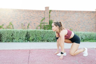 Kamu parkında koşmak için başlangıç pozisyonu alan kararlı genç kadının yan görünümü