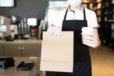 Erkek personelin elinde paket ve tek kullanımlık kahve fincanı var.