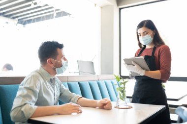 Kafedeki Coronavirus salgını sırasında maske ve eldiven takan garsona emir veren orta yaşlı bir adam.