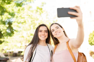 Parktaki akıllı telefondan arkadaşlarıyla selfie çeken genç bir kadın.