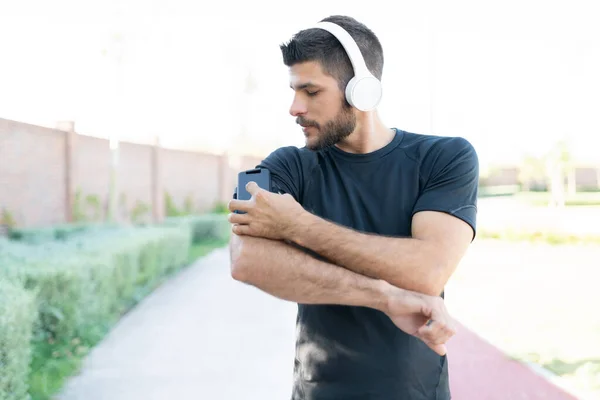 Sporty young man listening music through wireless headphones while working out in park