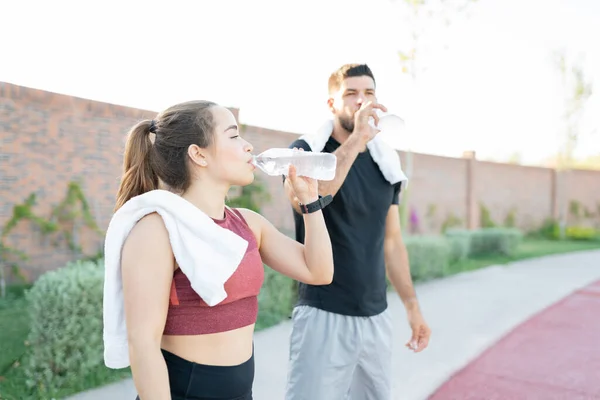 Exhausted young man and woman drinking water after exercising in park