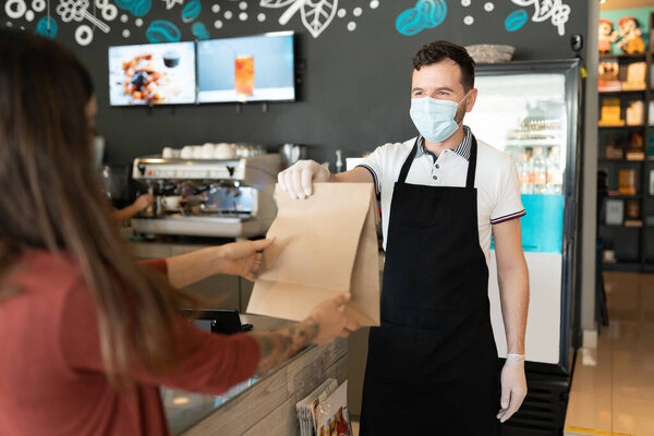 Male staff giving parcel to woman at counter during coronavirus outbreak