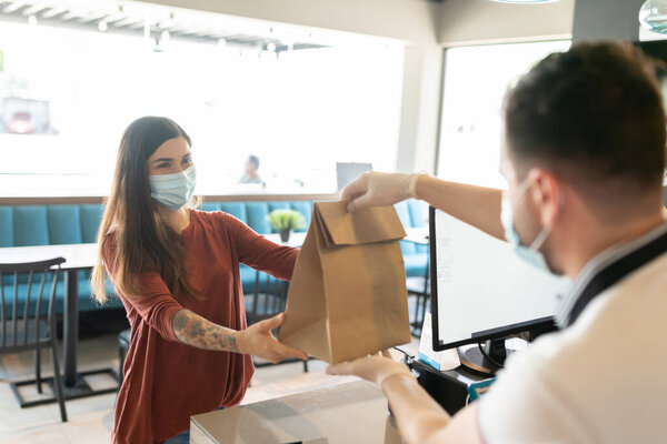 Latin young woman taking parcel from staff at takeaway counter in restaurant