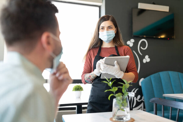 Latin young waitress taking order from customer during coronavirus crisis in coffee shop