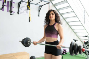 Çapraz antrenman sırasında halter kaldıran kendine güvenen genç kadın.