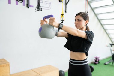 Çekici İspanyol zayıf kadın fitness kulübünde kettlebell ile egzersiz yapıyor.