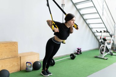 Sağlık kulübünde TRX bandosuyla egzersiz yapan kararlı Latin bir genç kadın.