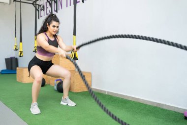 Savaş halatlarıyla antrenman yapan kararlı, sportif, İspanyol bir genç kadın.