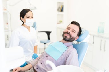 Kadın dişçi, klinikte sandalyeye oturmuş gülümseyen orta yaşlı bir adam.