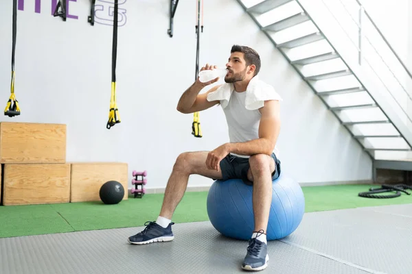 Erschöpfter Junger Mann Trinkt Wasser Während Auf Fitnessball Fitnessstudio Sitzt — Stockfoto