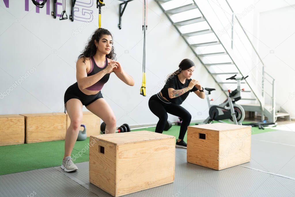 Confident sporty Hispanic young women doing jumping exercises at fitness club