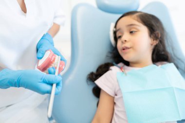 Kadın dişçi, İspanyol kıza klinikteki gülümseme tasarımı modelinde dişlerini nasıl fırçalayacağını anlatıyor.