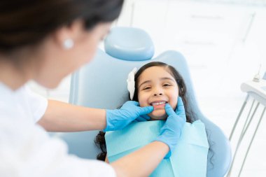 Kadın dişçi, diş kliniğinde küçük bir hastanın dişlerini kontrol ediyor.