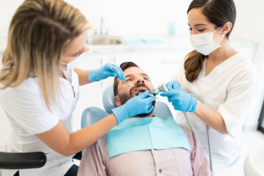 Klinikte diş tedavisi sırasında orta yaşlı bir adamı muayene eden iki dişçi.