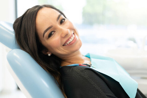 Крупный план улыбающейся привлекательной женщины среднего возраста, лежащей на стуле в стоматологической клинике