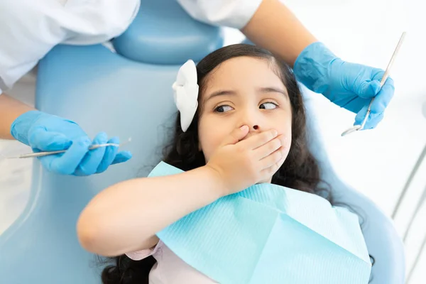 Garota Hispânica Assustada Cobrindo Boca Enquanto Dentista Segurando Ferramentas Durante — Fotografia de Stock