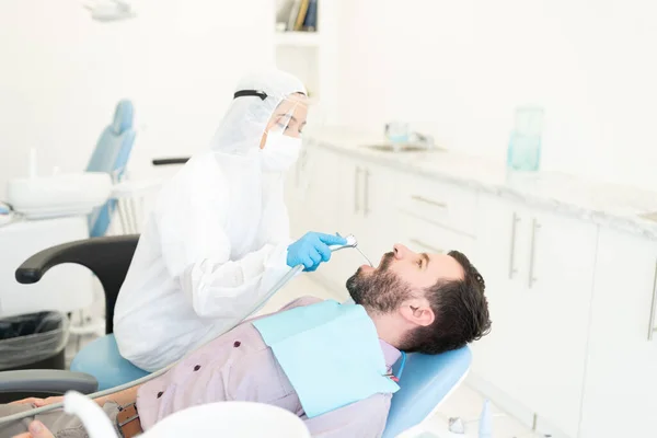 Kobieta Odontolog Zestawie Ochronnym Badający Zęby Człowieka Podczas Wybuchu Koronawirusu — Zdjęcie stockowe