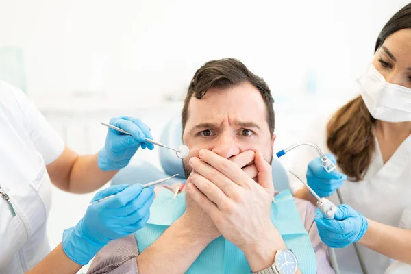 Hombre Adulto Medio Asustado Cubriendo Boca Mientras Dentista Sostiene Herramientas —  Fotos de Stock