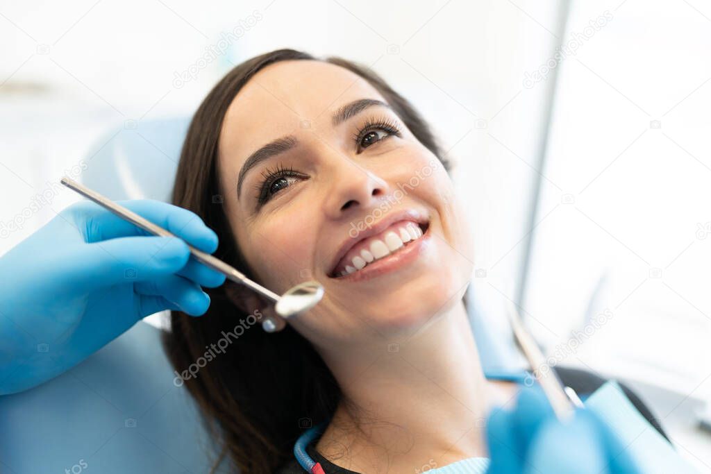 Dentist checking Caucasian woman with carver and mirror at dental clinic