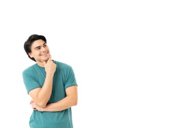 Düşünceli genç adam gülümsüyor ve elleri çenesinde dikilirken yukarı bakıyor.