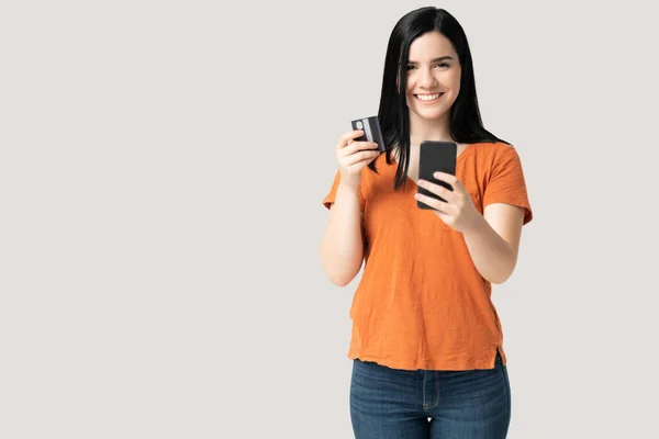 携帯電話を使いながらクレジットカードを持つ白人の若い女性の笑顔の肖像 — ストック写真