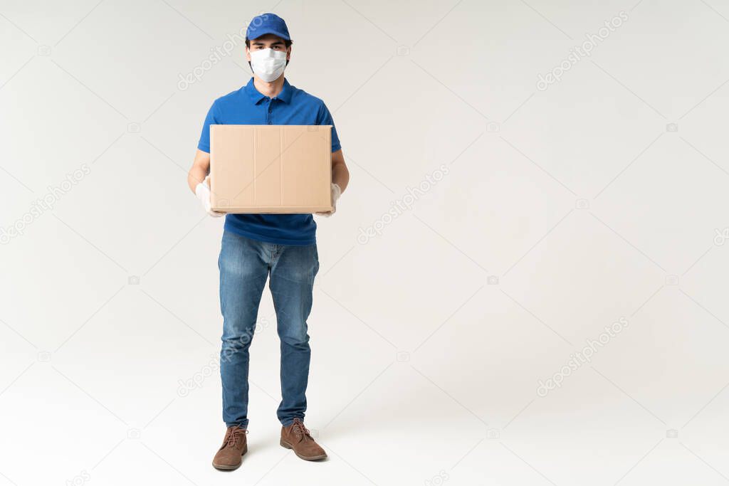 Delivery man in face mask carrying cardboard box during coronavirus crisis