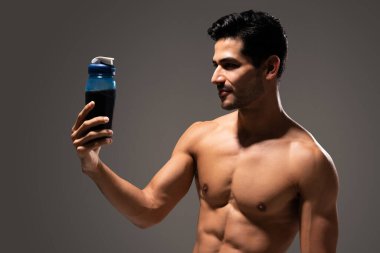 Şişedeki protein içeceğine bakan yakışıklı, üstsüz bir erkek atlet.