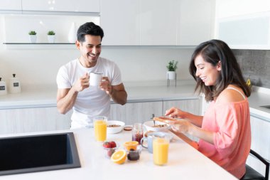 Mutlu erkek arkadaş kahve içerken kız arkadaş kahvaltıda reçel sürüyor.