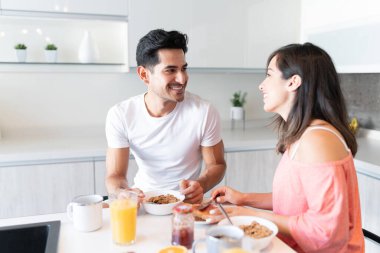 Gülümseyen genç çift mutfakta kahvaltı yapıyor.