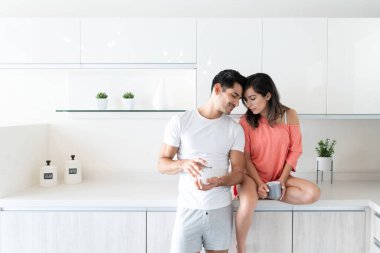 Romantik genç çift mutfakta kahve içerken kafalarına dokunuyor.