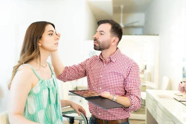 美容室で魅力的な女性にメイクを施しながらパレットを持つラテン男性Mua — ストック写真