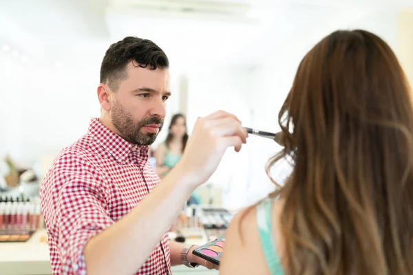 自信的男性化妆师在年轻女子的脸上涂上腮红 — 图库照片