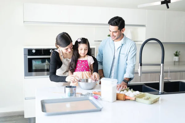 Mother and father guiding daughter in preparing food at home