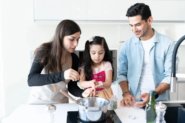 Latin parents teaching cute daughter to cook food at home