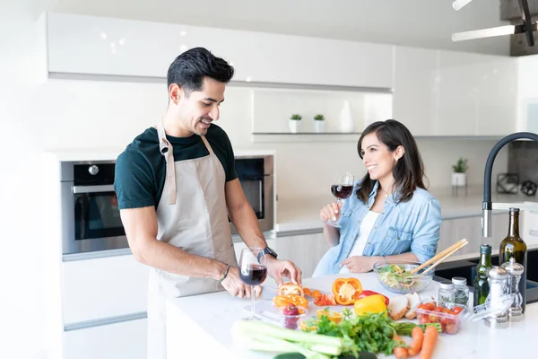 Mulher Sorridente Tomando Vinho Enquanto Conversa Com Namorado Cortando Legumes — Fotografia de Stock