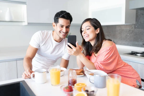 快乐的年轻夫妇一边在家里吃早饭 一边看智能手机 — 图库照片