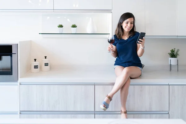 Giovane Donna Sorridente Con Vino Utilizzando Smartphone Mentre Seduto Sul — Foto Stock