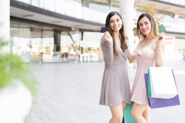 Gülümseyen çekici kadınlar alışveriş merkezinin karşısında dururken kredi kartı gösteriyorlar.