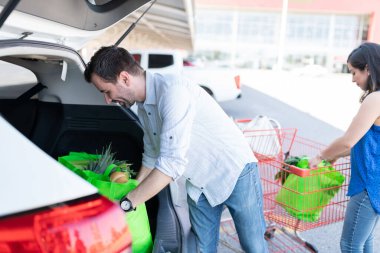 Otoparktaki araba bagajında alışveriş torbaları yükleyen çift.