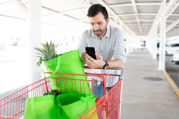 Man Checking Grocery List Smartphone While Standing Shopping Cart Parking — Stock Photo, Image