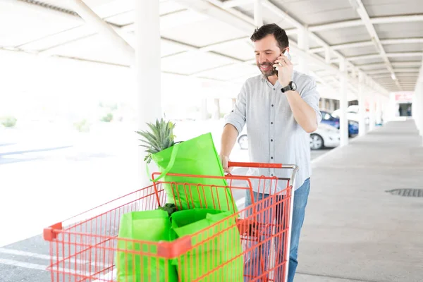 Spanisch Sprechender Mann Mit Smartphone Steht Mit Einkaufswagen Auf Parkplatz — Stockfoto