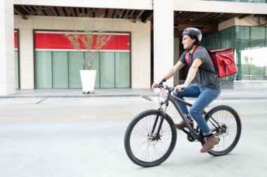 Sırt çantalı gülen bir teslimatçı sokakta bisiklet sürüyor.