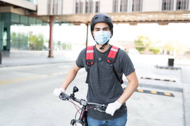 Sokakta bisikletle duran maskeli genç teslimatçı.