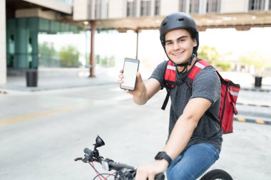 Bisiklette otururken akıllı telefon gösteren gülümseyen İspanyol kurye portresi
