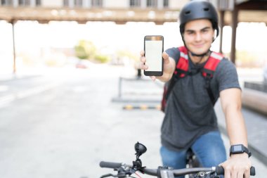 Bisikletle kurye getirirken akıllı telefon gösteren genç adam.