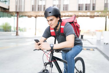 Akıllı telefondan bisiklet sürerken harita kullanan yakışıklı teslimatçı.