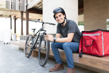 Sırt çantasında otururken mobil uygulama kullanan kendinden emin bir teslimatçı.