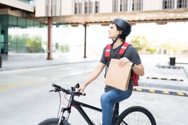 Bisikletli, gülümseyen genç teslimatçı. Sokakta parsel taşıyor.