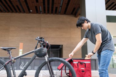 Bisikletle sırt çantasından paketi çıkaran genç teslimatçı.